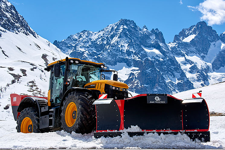 Engin équipé d'une lame tri-axiale en action sur une route de montagne enneigée